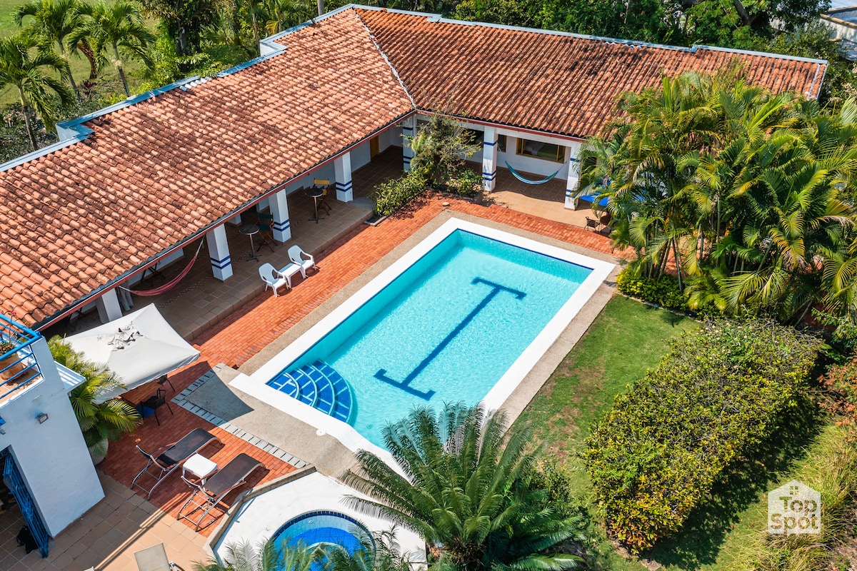 A bird's eye view captures a serene outdoor space featuring a private pool surrounded by brick-paved areas. A hot tub is positioned nearby, and lush greenery and palm trees enhance the tranquil setting. Hammocks and lounge chairs provide comfortable areas for relaxation.