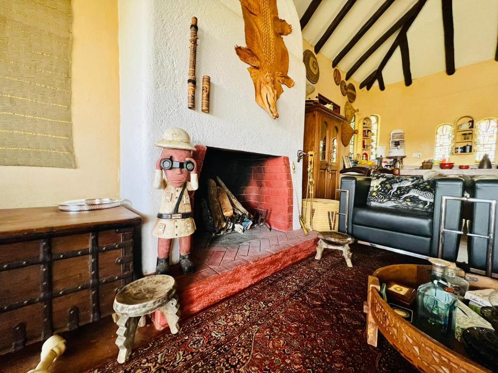 A welcoming living area features a traditional fireplace with stacked firewood, flanked by decorative sculptures. The textured rug adds warmth to the space, while wooden accents and dark leather seating complement the inviting ambiance. Tall windows allow natural light to brighten the room.