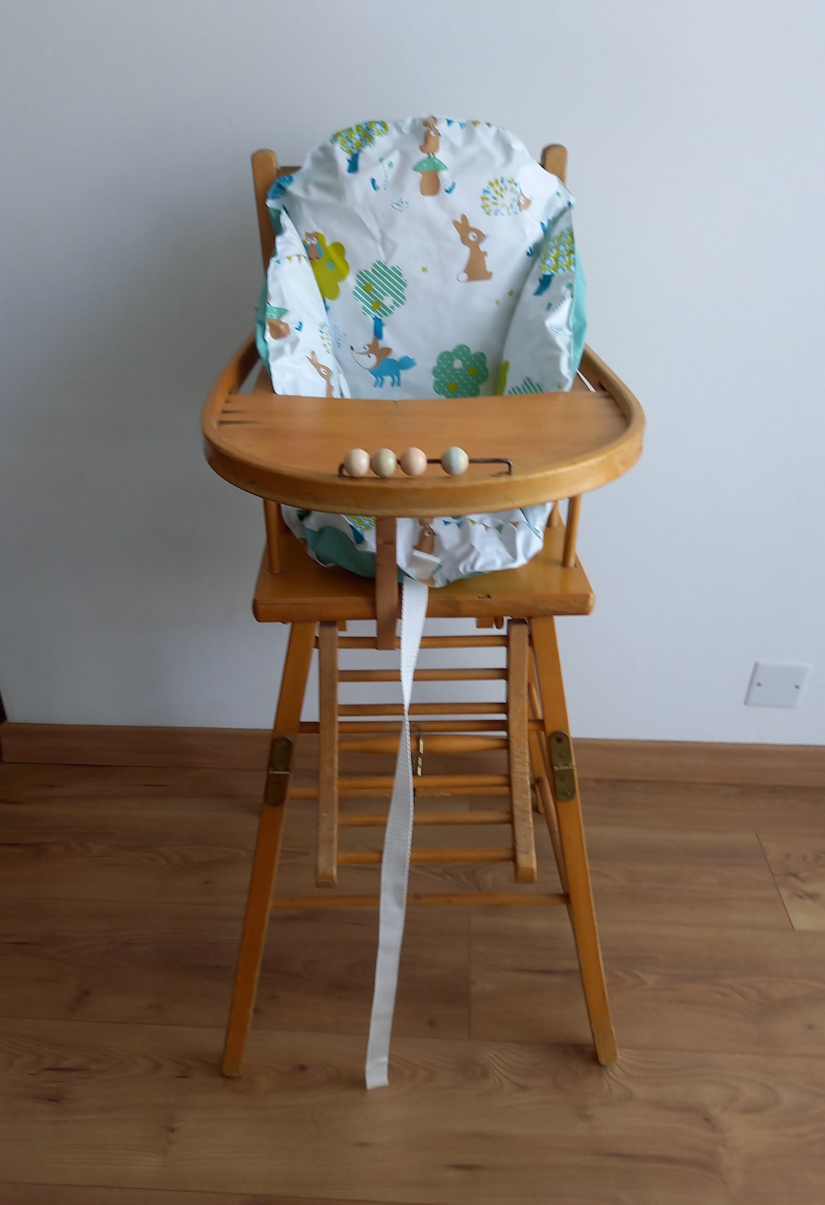 A wooden high chair is presented, featuring a cushioned seat covered in a colorful animal print fabric. The tray is empty, and safety straps are visible, providing stability for a child during mealtime.