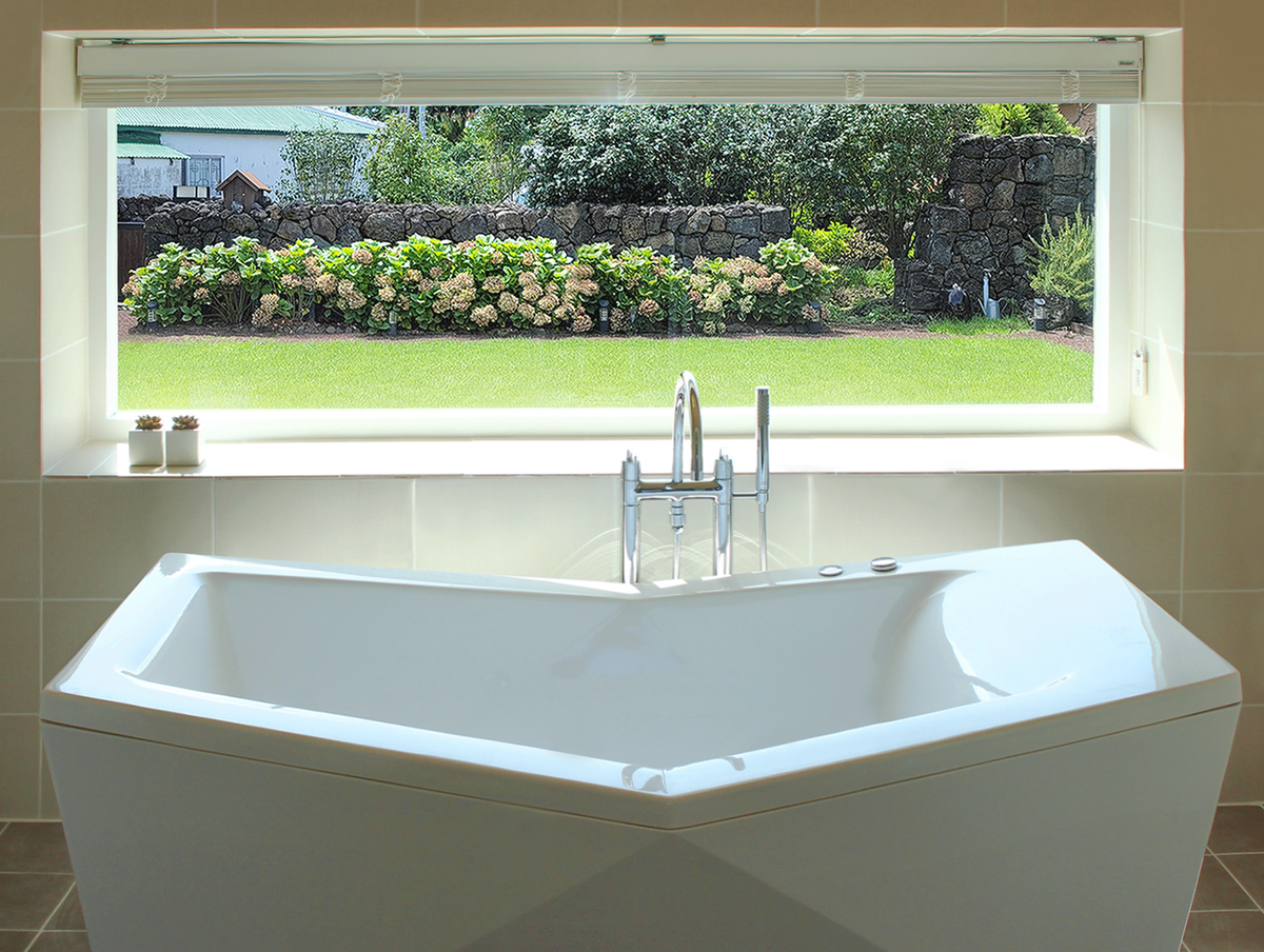 A modern, soft bathtub is positioned beneath a large window, allowing natural light to illuminate the bathroom. The view showcases a vibrant garden with blooming flowers and lush greenery, providing a serene backdrop for relaxation.
