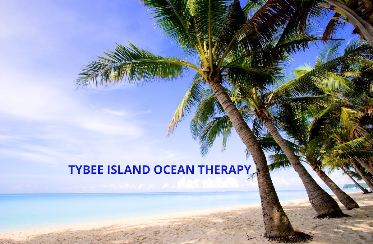 Palm trees are positioned along a sandy beach, reaching toward a clear blue sky. Calm ocean waters stretch toward the horizon, inviting a sense of serenity and relaxation. The beach is gently curved, demonstrating a picturesque coastal environment.