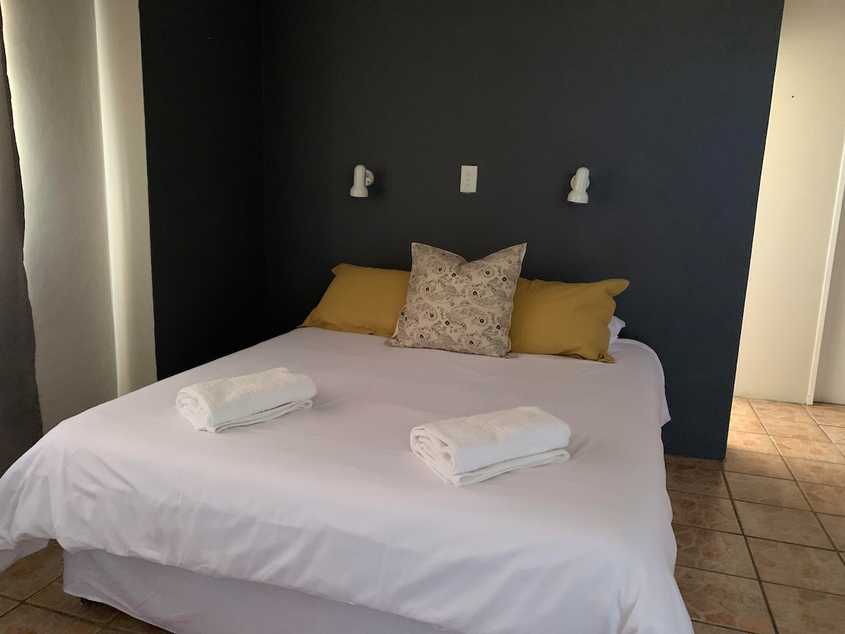 A spacious bed is centered in the room, adorned with two decorative pillows and fresh white towels neatly placed on the covers. The wall behind features a deep gray color, creating a calming backdrop against the light-colored bedding.