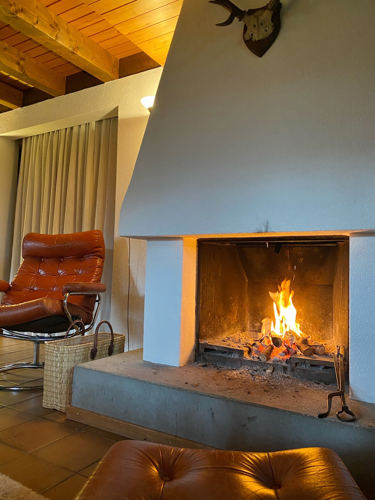 A cozy living area features a modern armchair next to a stylish fireplace. Flames dance within the fireplace, providing warmth. Soft light is cast onto the textured walls, while neutral drapes frame the window, enhancing the serene ambiance of the room.