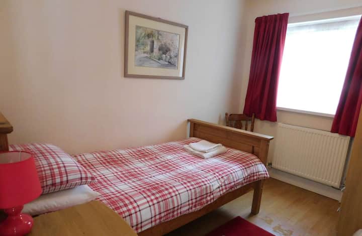 חדר שינה יחיד עם ארון בגדים בגובה מלא, ארון ליד המיטה עם מנורת קריאה ונוף לגינה האחורית.