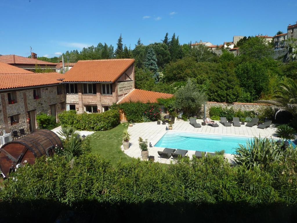 An expansive view showcases the outdoor area, featuring a rectangular pool surrounded by sun loungers. Lush greenery and mature trees provide a natural backdrop for the stone building with a terracotta roof, while a covered area is visible to the left.