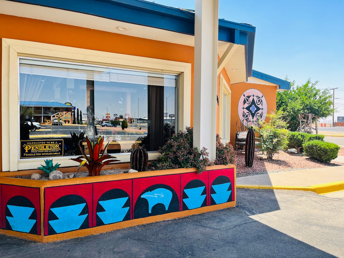 A colorful exterior features a bright orange wall with a geometric mural. Decorative plants are arranged along a painted stone ledge, while the entrance showcases a large window that invites natural light into the space.