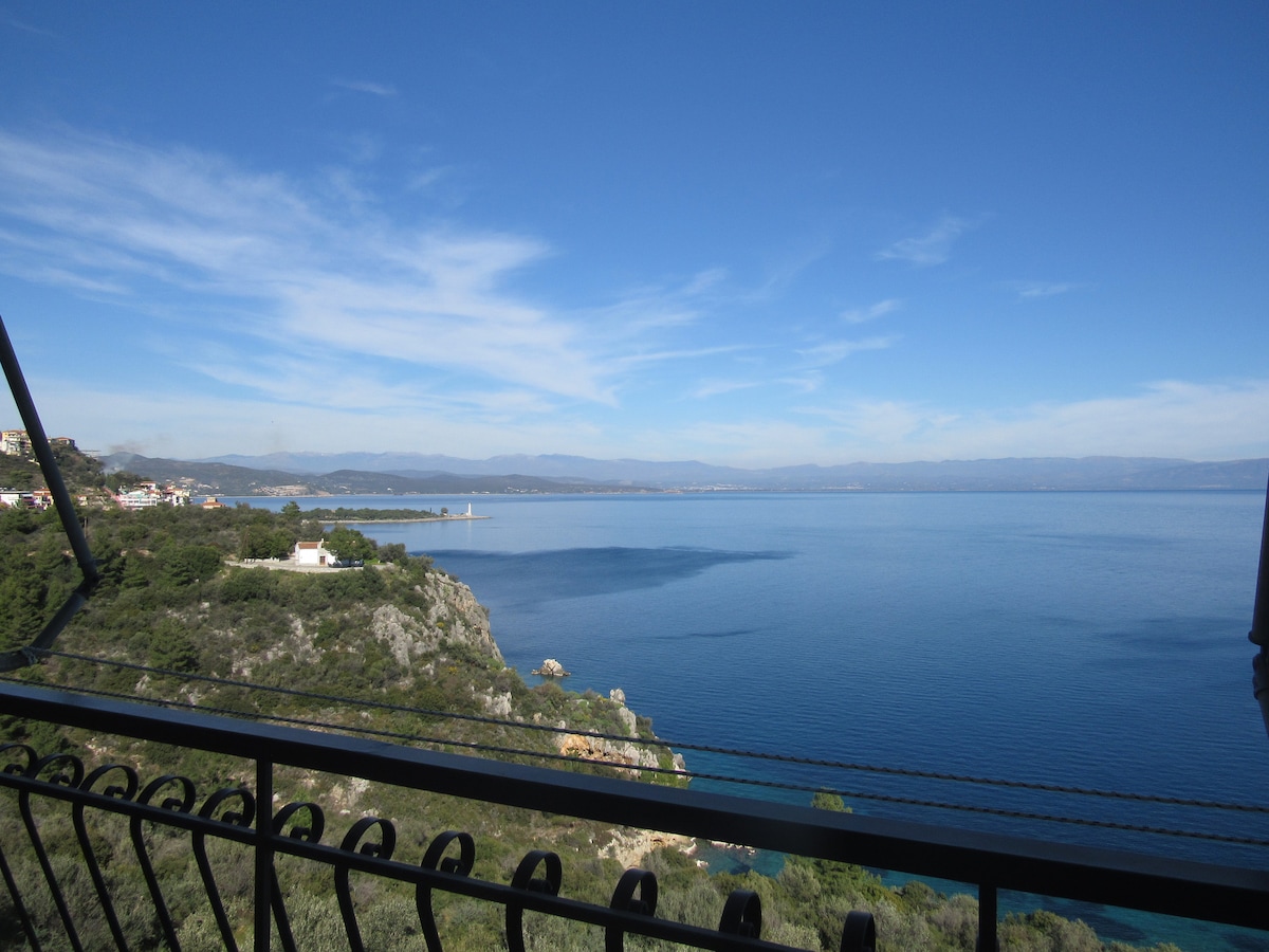 A panoramic view of the tranquil sea is presented, with gentle waves lapping against the shore. Rolling hills are visible along the coastline, framed by a clear blue sky. The scene is enriched by the distant mountains, creating a serene landscape that invites relaxation.