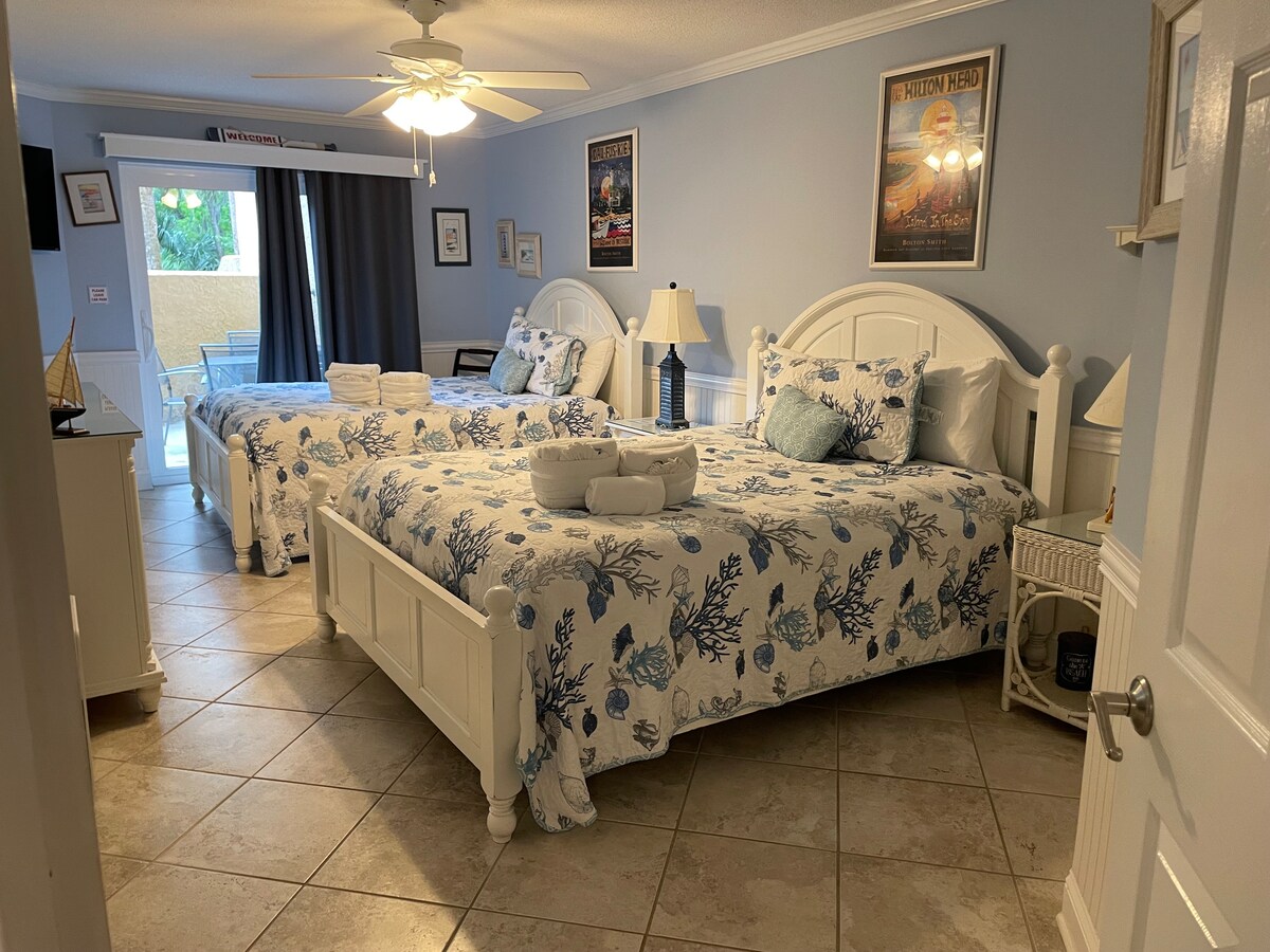 Dormitorio con dos camas tamaño queen y TV y puerta de vidrio al patio.