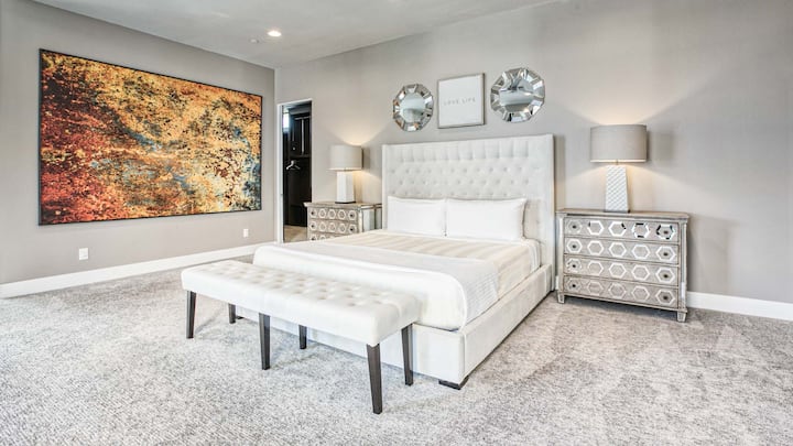 Amplio dormitorio, una cama tamaño king con baño, cabecera con mechones, iluminación suave y decoración moderna.