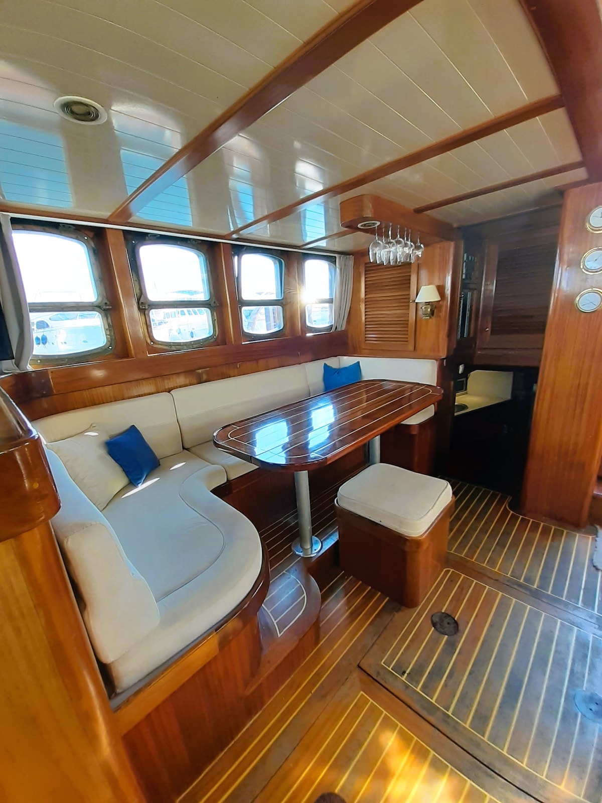 The interior features a cozy dining area with elegant wooden details. A polished table is surrounded by a U-shaped sofa, complemented by a small stool. Large windows allow natural light to fill the space, enhancing the inviting atmosphere of the cabin.