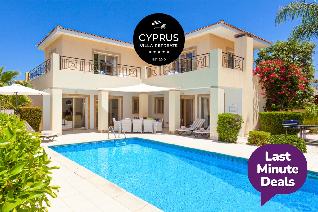A modern villa is showcased with a clear blue swimming pool in the foreground, surrounded by a tiled patio. The structure features large glass doors and a balcony with decorative railings. Lush greenery and colorful plants frame the property, enhancing the inviting setting.
