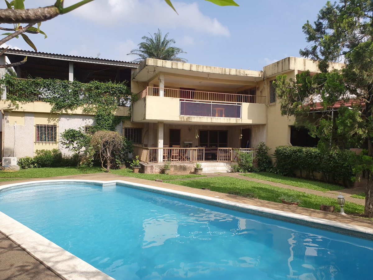 The photo captures a well-maintained building overlooking a swimming pool. Lush greenery surrounds the property, with a deck and ample outdoor space for relaxation. Bright blue skies complement the inviting atmosphere, enhancing the serene environment of the residence.