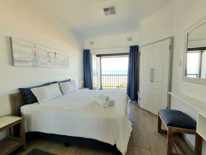 ห้องนอนหลักมีเตียงควีนไซส์และห้องน้ำในตัว เปิดออกสู่ดาดฟ้าที่มีวิวชายหาดที่ไม่มีสิ่งกีดขวาง