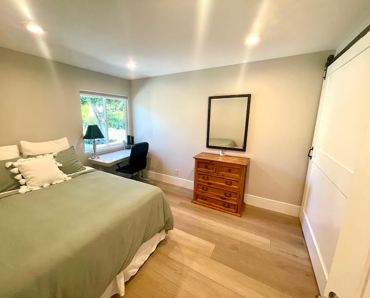 El dormitorio de invitados con cama tamaño queen tiene un escritorio de ajuste de altura con vista a la ventana al patio trasero.