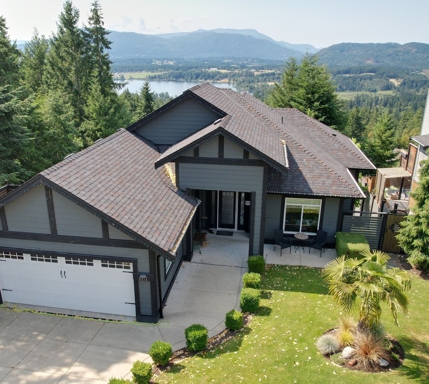 The exterior of the modern suite is highlighted by a well-maintained lawn and a spacious driveway. Surrounded by trees, the home offers beautiful views of Quamichan Lake and the mountains beyond, creating a serene atmosphere.