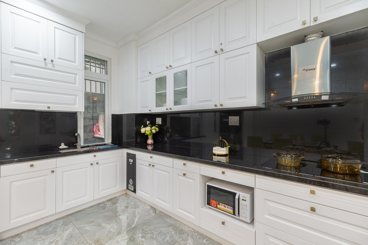 A modern kitchen features sleek white cabinetry complemented by dark granite countertops. Stainless steel appliances are prominently displayed, including a gas stove with an overhead hood. Natural light filters in through a window, illuminating the organized space.