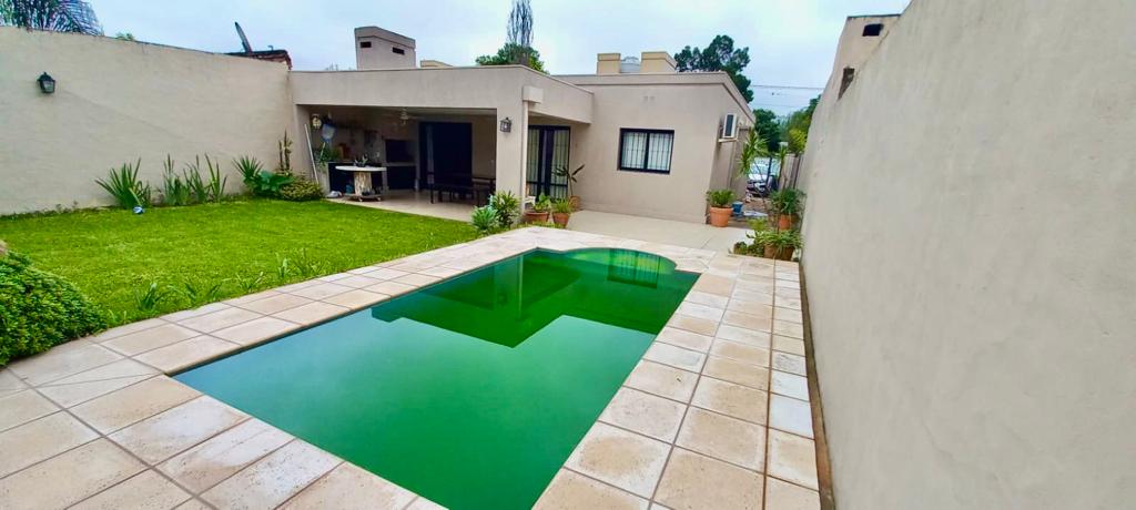 A private outdoor area showcases a swimming pool surrounded by spacious tiled patio and well-maintained green garden. The house features an open layout, with large windows that connect the indoor and outdoor spaces.