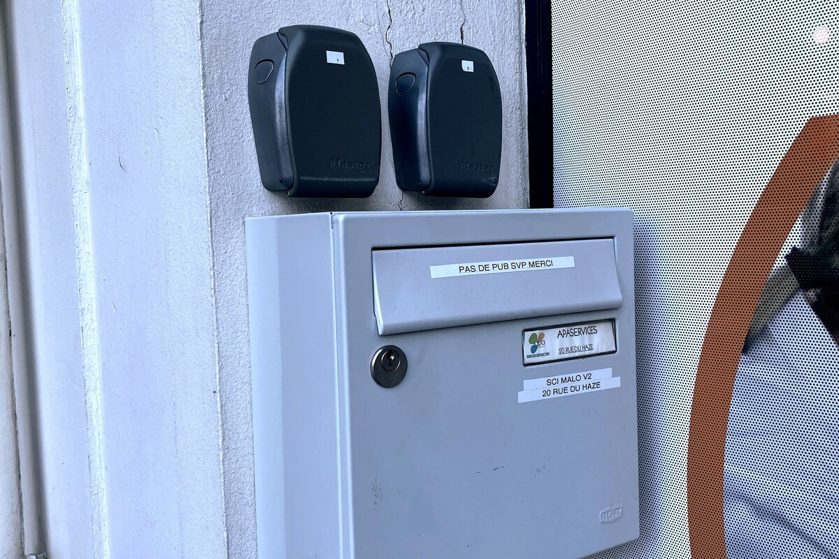 The image displays a secure mailbox mounted on a wall, complemented by two access key fobs positioned above it. Clear labeling is seen on the mailbox, providing essential information for guests.