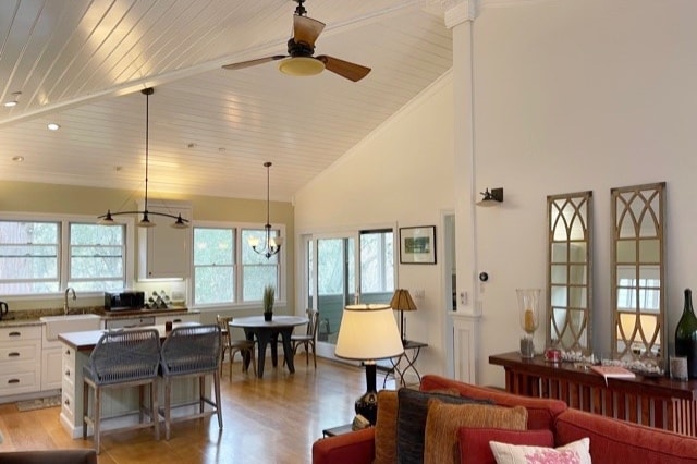 An open great room features high ceilings with exposed beams, a spacious dining area, and a modern kitchen. Natural light floods in through multiple windows. Comfortable seating includes a red couch and a decorative lamp, enhancing the inviting atmosphere.