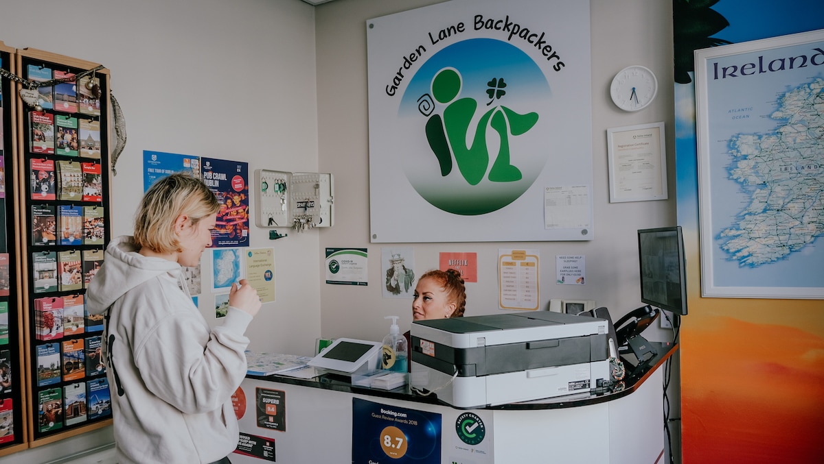 The reception area is designed for guest check-ins, featuring a service desk and informational signage. A promotional display showcasing local attractions occupies one wall. A clock and various brochures are visible, providing resources for guests exploring the area.