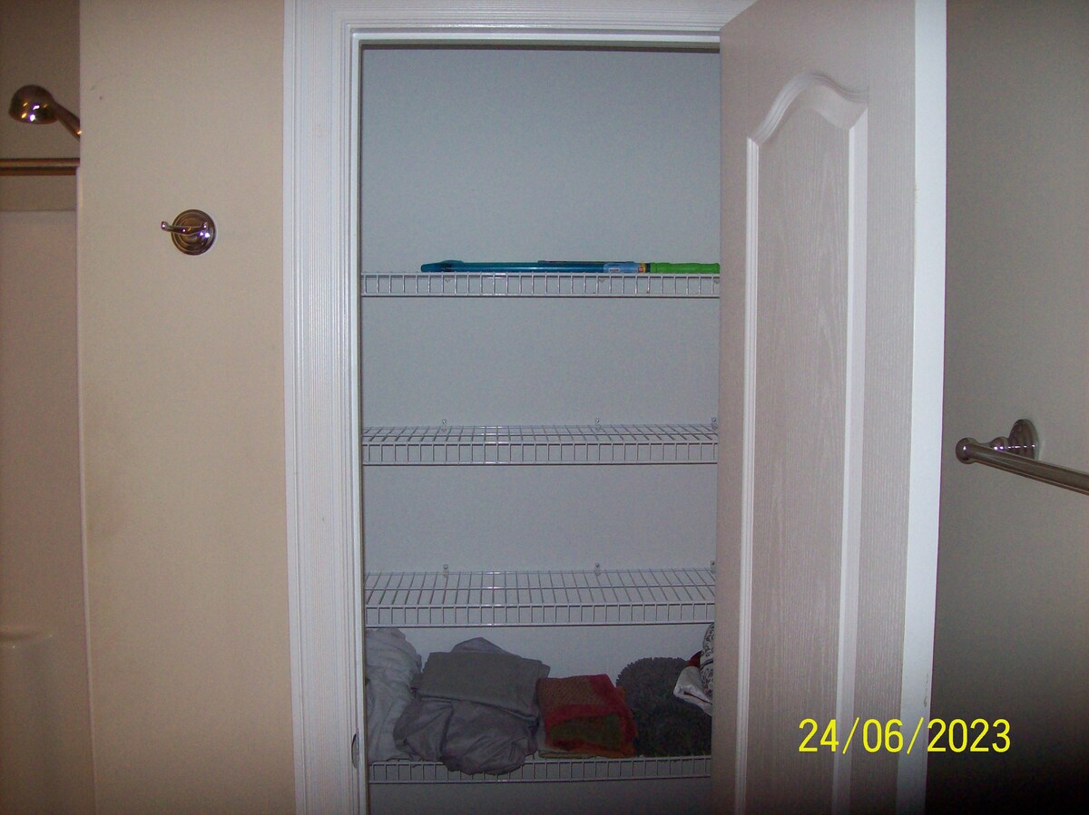 A closet is displayed with several wire shelves, featuring neatly organized items. On the lower shelf, towels are arranged, while the upper shelves are mostly empty except for a few items. The closet door is open, allowing a clear view of the interior.
