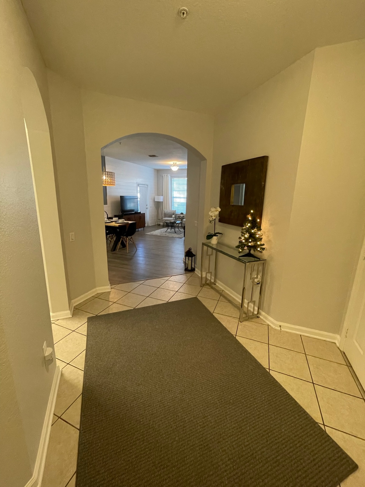 A welcoming entryway is highlighted by a spacious hallway with tiled flooring. An archway leads to the open living area, visible in the background. A console table with decorative items stands to the right, while soft lighting illuminates the space.