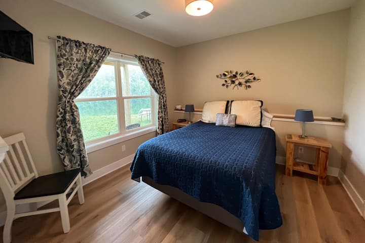 Queen sized bed with a view of the lake and a TV. 