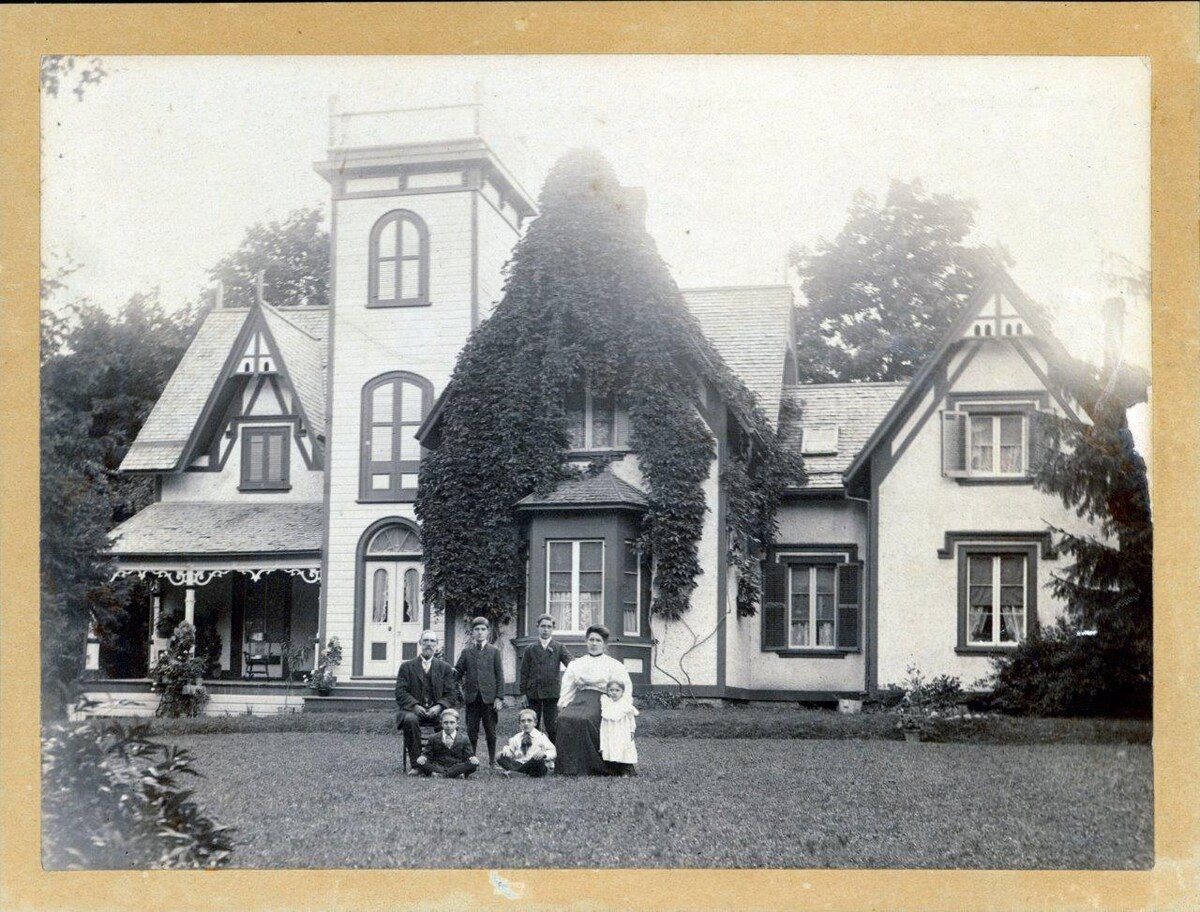 The historic home features a large facade adorned with lush ivy, highlighting its Victorian architecture. A well-kept lawn surrounds the building, providing a picturesque setting. The distinct shapes of the windows and rooflines emphasize the home's charm and historical significance.