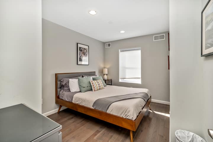 Serene retreat with soft gray tones, natural light and a sleek wooden bed for a warm and restful atmosphere.