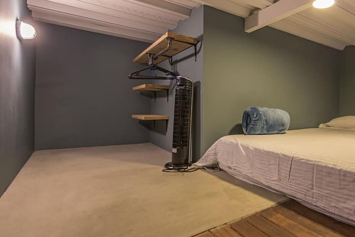Dormitorio con cama doble, armario con perchas y ventilador portátil.