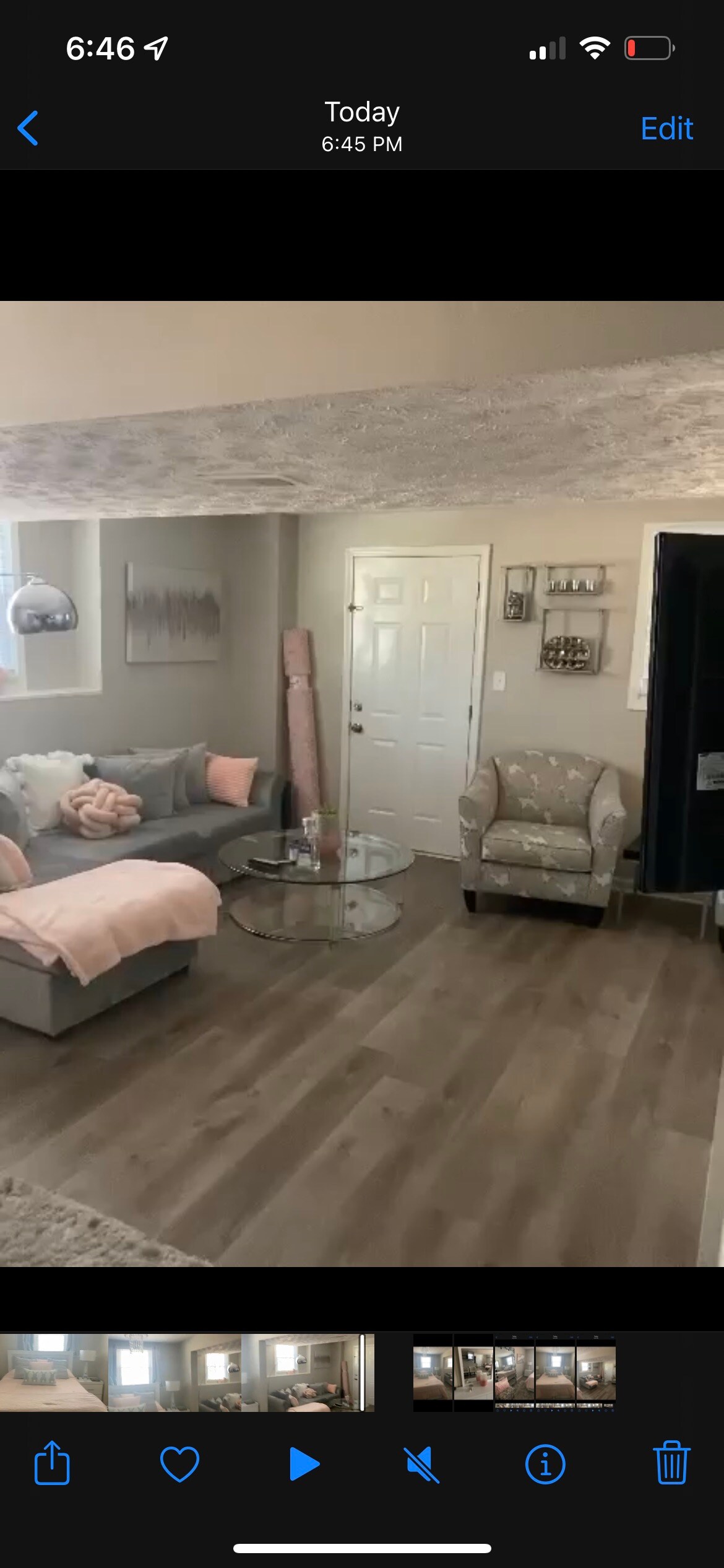 A cozy living area is featured with a light gray sectional sofa adorned with soft pink throw pillows. A round glass coffee table is positioned centrally, while a patterned accent chair sits to the side. Natural light brightens the space through a nearby window, enhancing the welcoming environment.