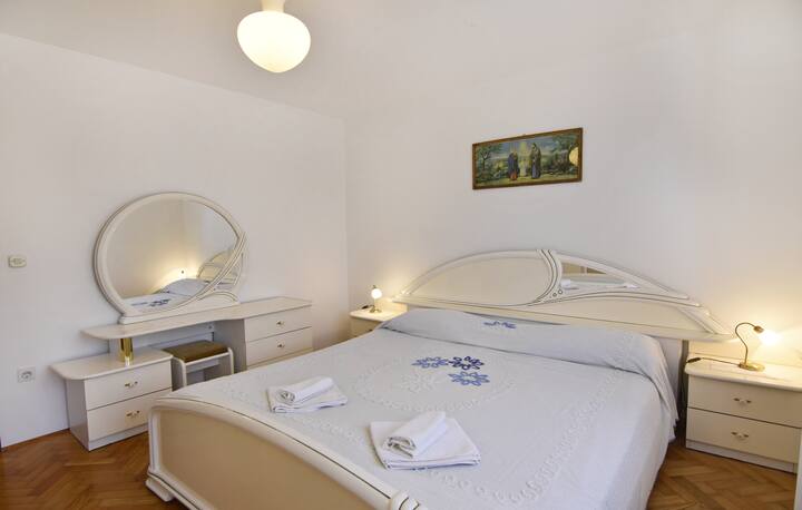 Dhoma e gjumit me krevat dopio, dy tavolina pranë krevatit me abazhurë nate, pasqyrë