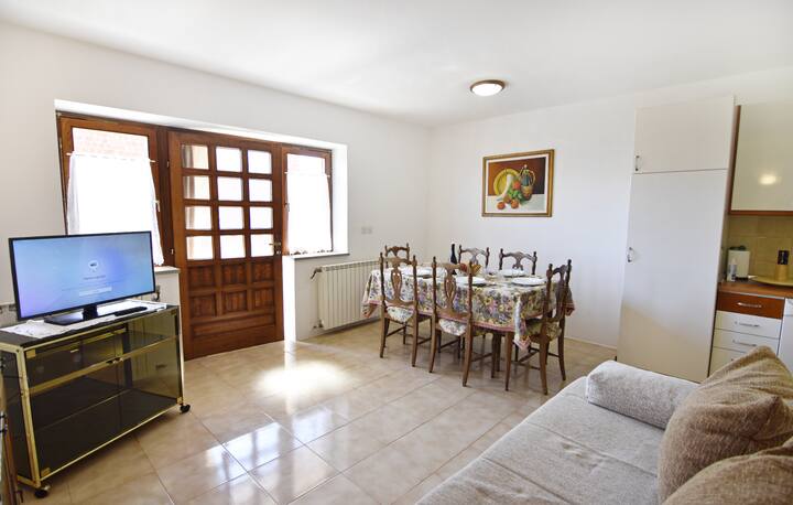 Ambienti i ndenjjes me divan krevat, tavolinë ngrënieje, televizor satelitor me ekran të sheshtë