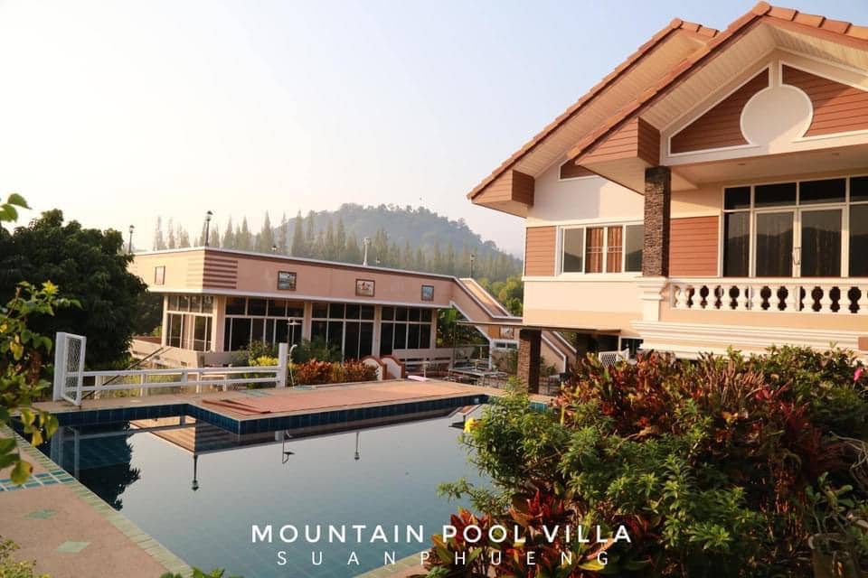 A private pool is surrounded by a landscaped garden, embraced by mountains in the background. The villa's exterior features a combination of modern and traditional architectural elements, including balconies and large windows that invite natural light.