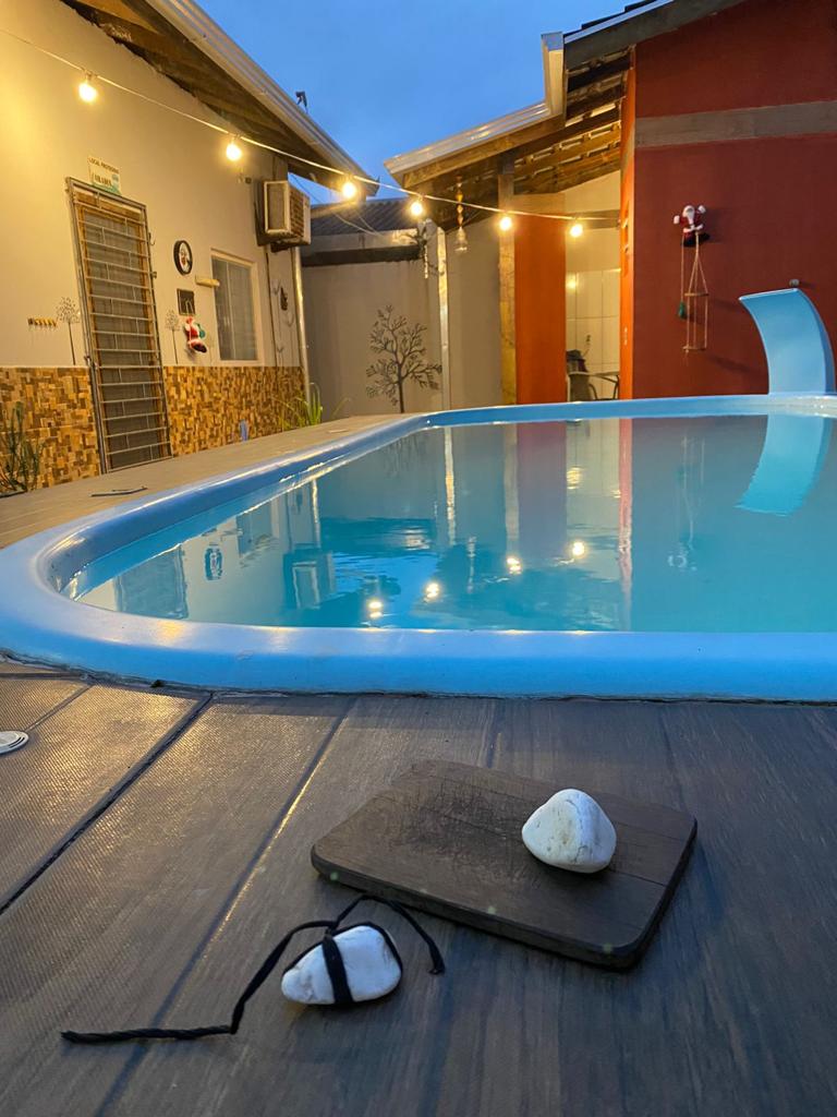 A tranquil pool area is illuminated by soft outdoor lights. The crystal-clear water reflects the surrounding architecture. A wooden board rests beside two smooth stones, creating a calm focal point on the pool deck.
