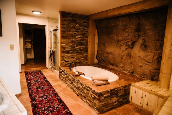Master bath with large tub surrounded by natural red rock, two head shower, double sink and extra storage