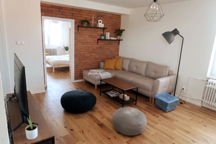 Поглед кон главниот простор во дневната соба.  Пространиот кауч е надополнет со масичка за кафе, подна ламба, ѕидни полици, отоман и телевизор. Совршено за забавување и уживање во благосостојбата. 