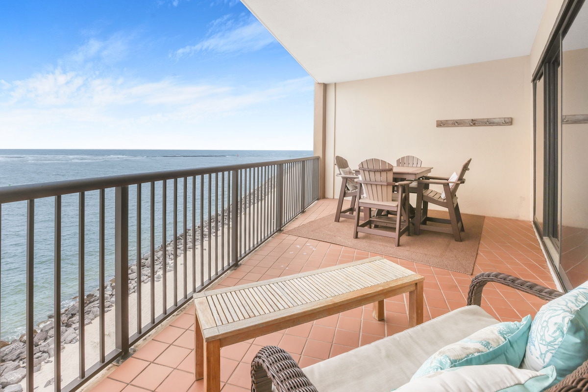 A spacious balcony features a dining table with seating for four, complemented by a cozy lounge chair. The view overlooks the serene waters of the Gulf of Mexico, providing an inviting space for relaxation and enjoyment of the surrounding scenery.