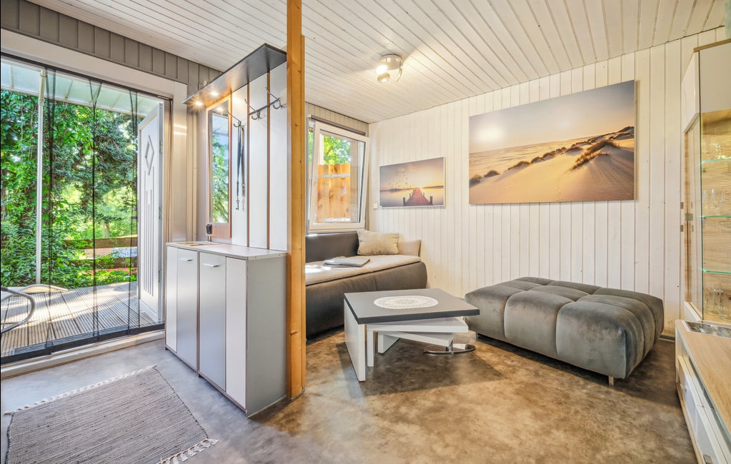 A bright living area is enhanced by large windows that invite natural light. Comfortable seating options are arranged around a modern coffee table. Light-colored walls and a neutral color palette create a soothing ambiance, while artwork depicting serene beach scenes adds visual interest.