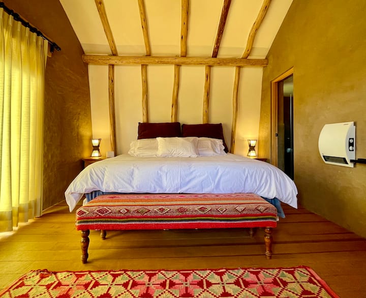 Wake up in your king master suite beneath soaring vaulted timber beams — crisp white linens, warm Andean lighting and a hand-woven Peruvian bench create the perfect sanctuary.