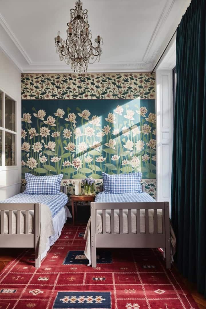 A second bedroom, featuring hand painted wallpaper by Idarica Gazzoni, an 19th century chandelier from Italy, a carpet from Morocco, and a peekaboo window into its bathroom 
