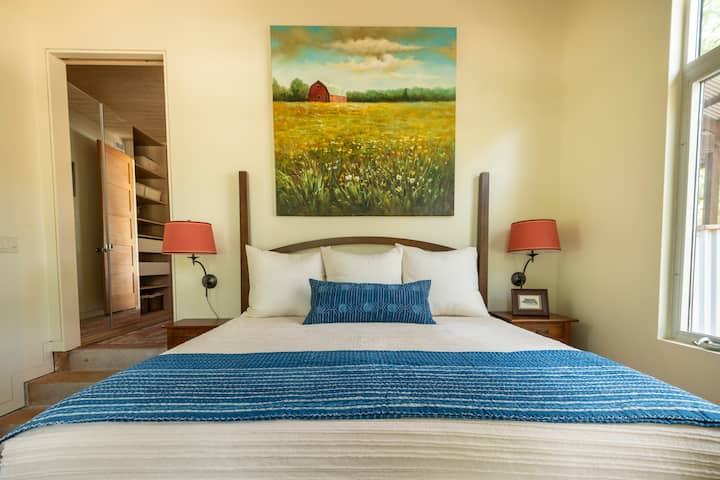 Საძინებელი №2 დიდი საწოლითა და სამუშაო მაგიდით, რომელიც აღჭურვილია დიდი მონიტორით, ერთმანეთთან დამაკავშირებელი კაბელებითა და სკამით.