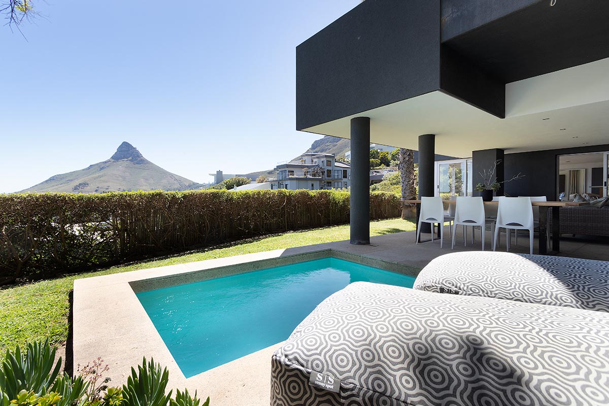 A private plunge pool is framed by manicured greenery, with sun loungers positioned nearby. A mountain rises majestically in the background, complementing the clean lines of the modern villa. The outdoor space invites relaxation and enjoyment of the scenic surroundings.