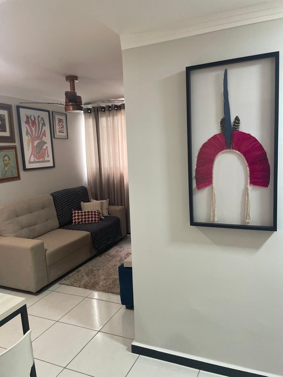 A living area features a beige sofa with decorative cushions, complemented by a patterned throw. Artwork decorates the walls, including a framed piece with vibrant colors. Natural light enters through sheer curtains, illuminating the space and enhancing the neutral decor.