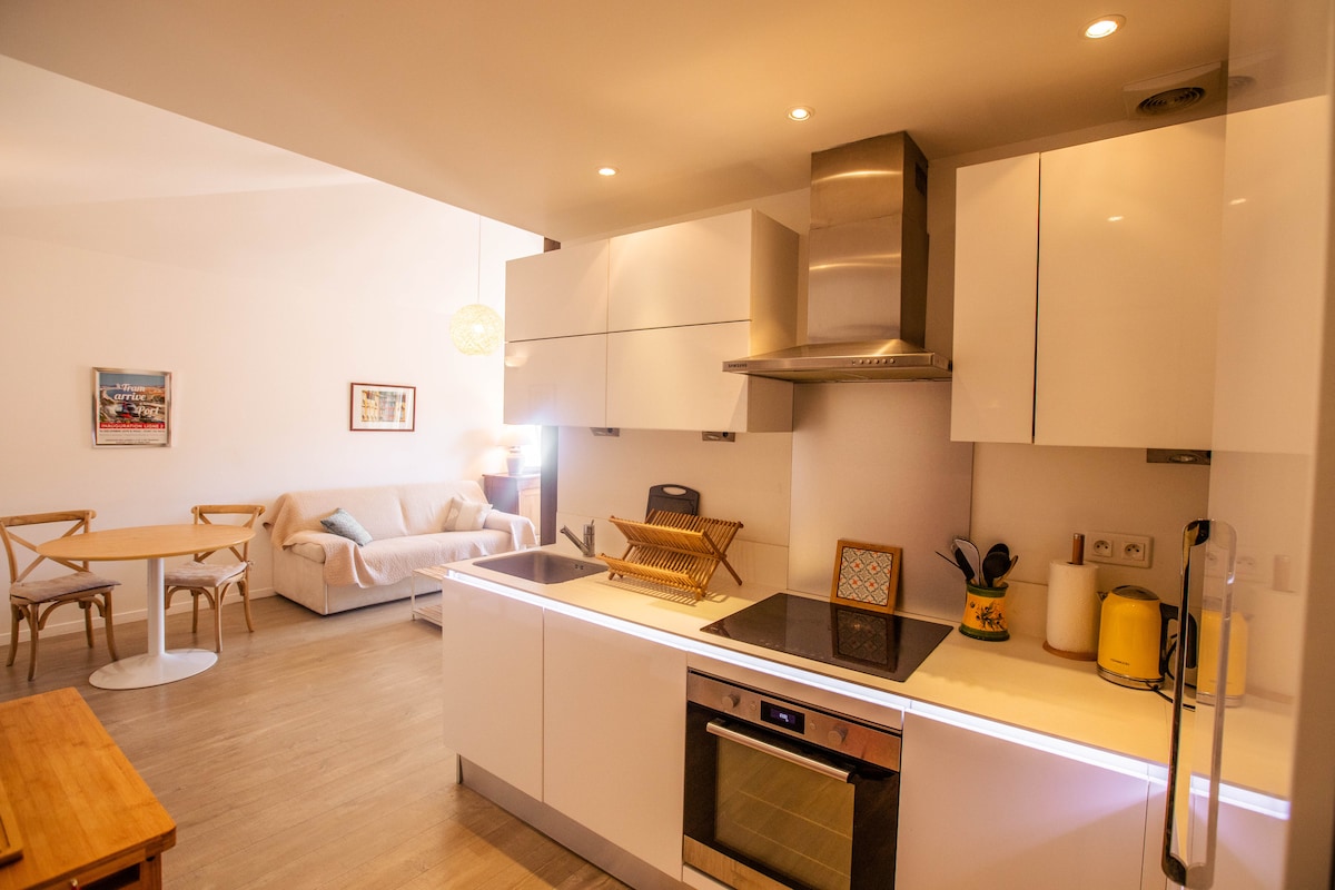 A modern kitchen is featured, equipped with sleek white cabinetry and stainless steel appliances. A dining area is visible, furnished with a round table and light wooden chairs. A cozy sofa adds comfort, inviting relaxation in the open space.