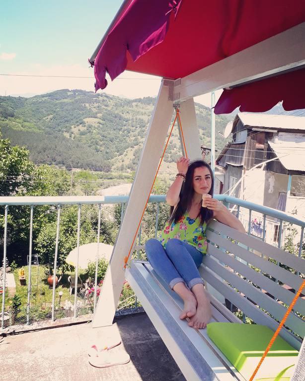 A swing seat is observed on a balcony, offering a view of the surrounding mountains and greenery. The area is enhanced by a vibrant awning and includes a cozy seating arrangement for relaxation. Natural light brightens the space, creating an inviting outdoor environment.