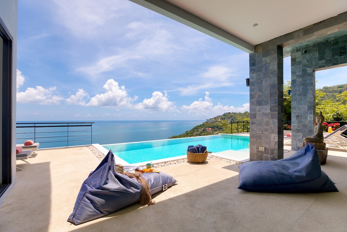 A spacious terrace area overlooks the infinity pool, with stunning views of the sea and sky. Soft bean bags are arranged invitingly nearby, while the smooth tiled floor complements the modern architecture and serene atmosphere of the villa.