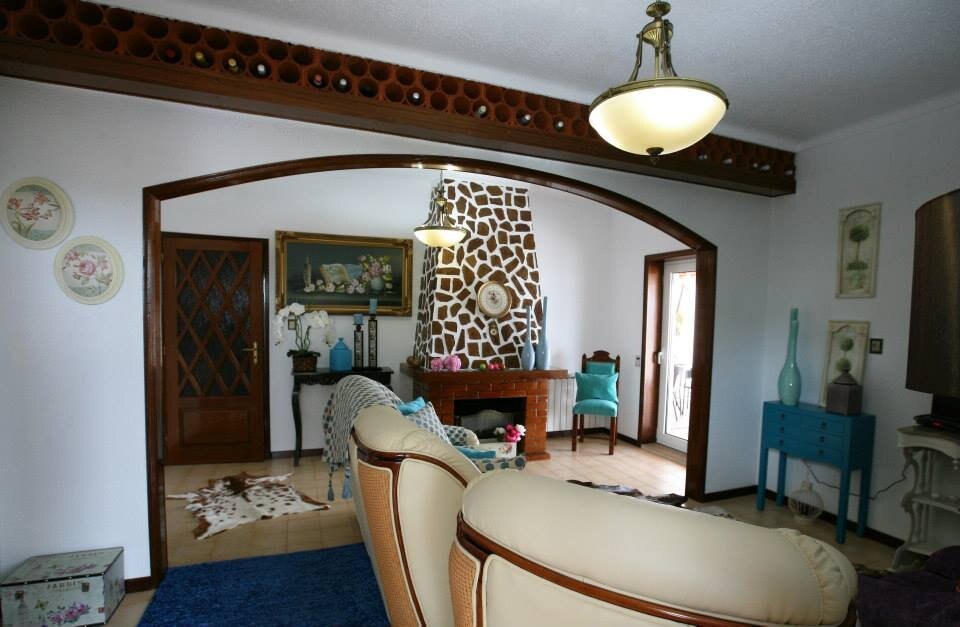 A spacious living area is characterized by arched doorways and a decorative wall design. Vintage furnishings, including a blue accent chair and a wooden console table, complement the natural light coming through the open doors, creating an inviting space for relaxation.