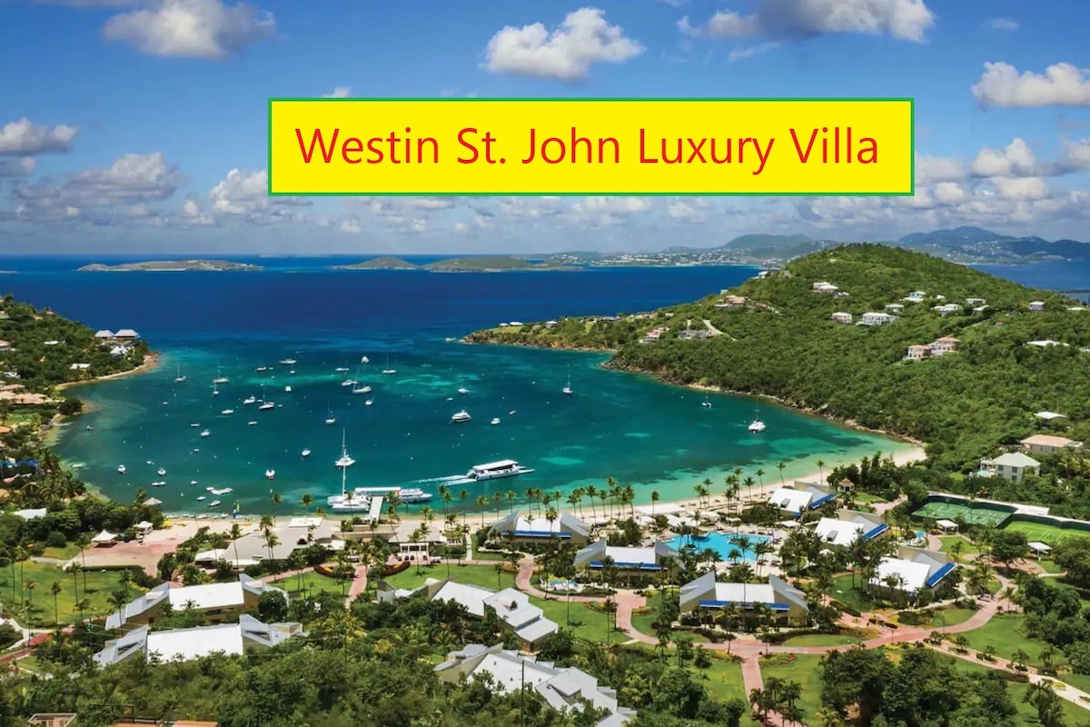 An aerial view of Westin St. John showcases the villa nestled along the picturesque coastline. Gentle waves lap against a sandy shore, while boats dot the emerald waters. The resort's lush greenery and well-kept grounds are visible, contributing to the serene, tropical environment.