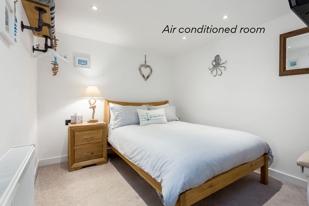 A well-lit bedroom features a spacious bed with light bedding and a decorative headboard. A bedside table with a lamp complements the cozy atmosphere. Wall decorations include nautical-themed accents, while a mirror adds depth to the room.